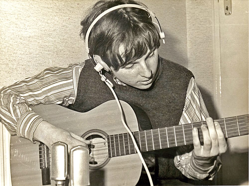 Michael O'Kelly as a young man in 1966, wearing headphones and playing classical guitar in a London recording studio.