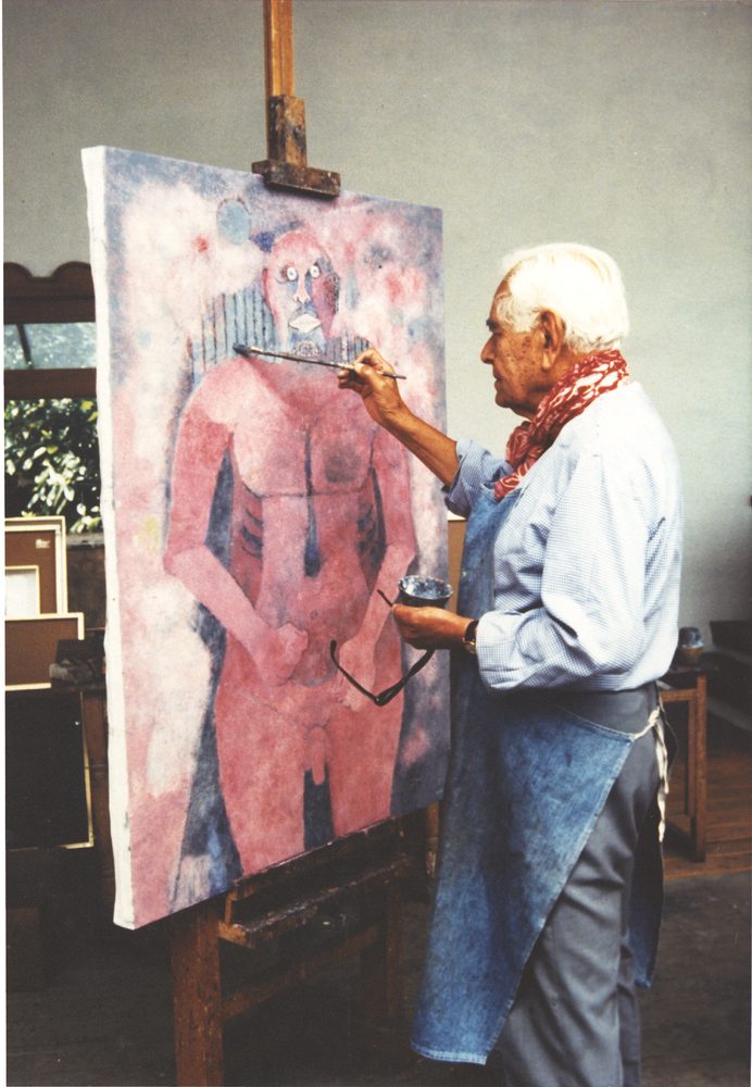 Rufino Tamayo, white-haired and in an apron, painting a large red figure on a canvas at his easel.