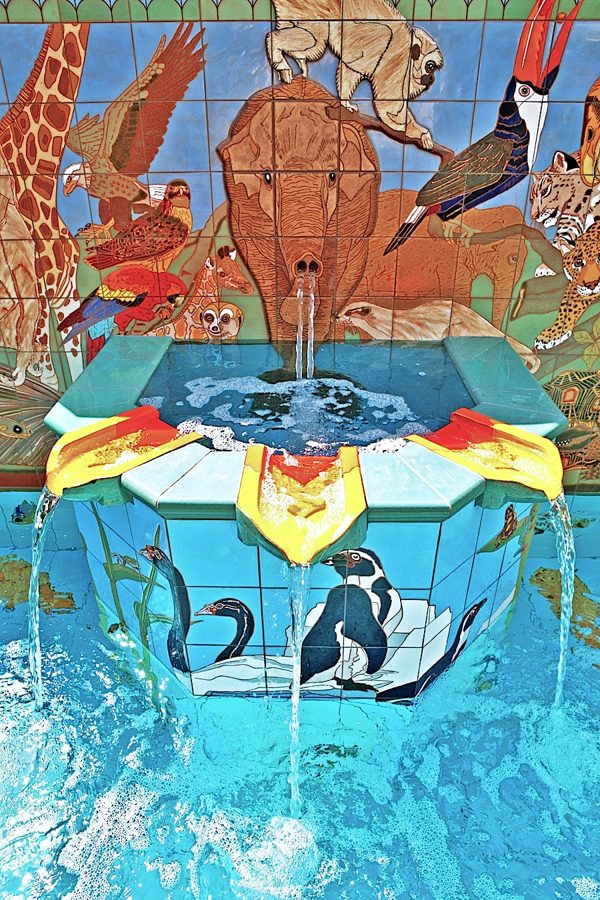 Detail: the fountain's central plinth, tiled with penguins on white rocks and a black swan among reeds, water falling from its lip.