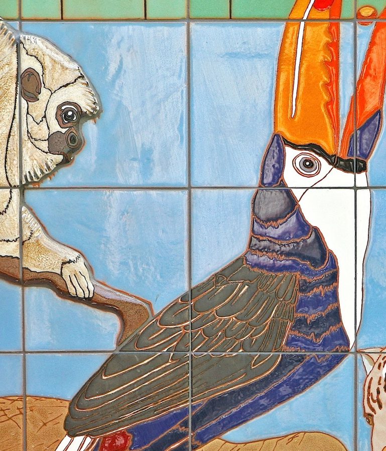 Detail: a toucan with an orange bill perched on a branch, beside a pale monkey peering from the tile.