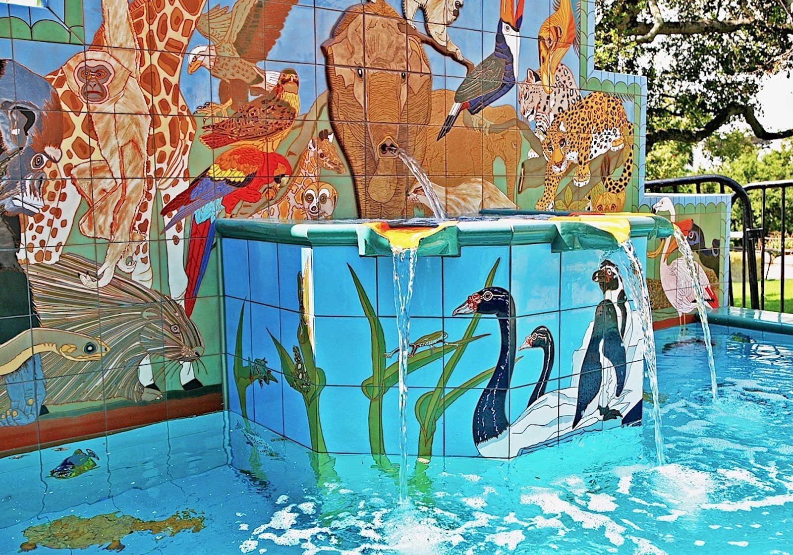The finished fountain seen close, water falling from the elephant's trunk onto the penguin plinth, the animals of the wall behind.
