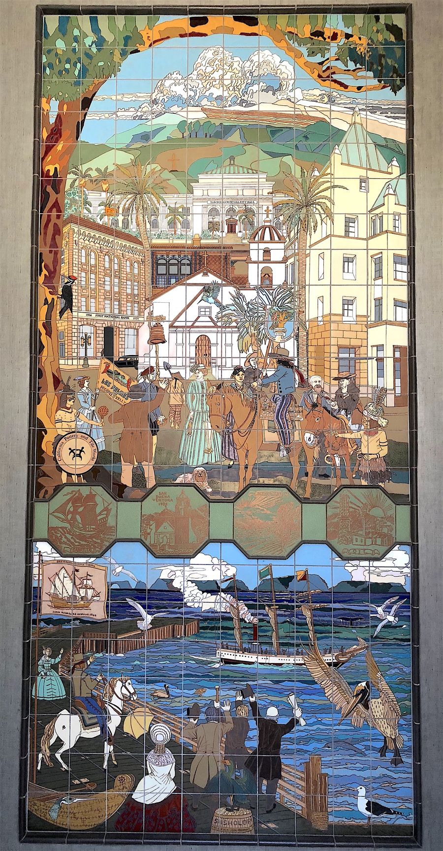 Las Palmas by Michael O'Kelly: a tall hand-glazed ceramic tile mural. A nineteenth-century Ventura street scene under an arch of foliage sits above a band of oxide-green octagonal medallions, above a harbour scene with a coastal steamer, pelicans and a crowd on the timber wharf.