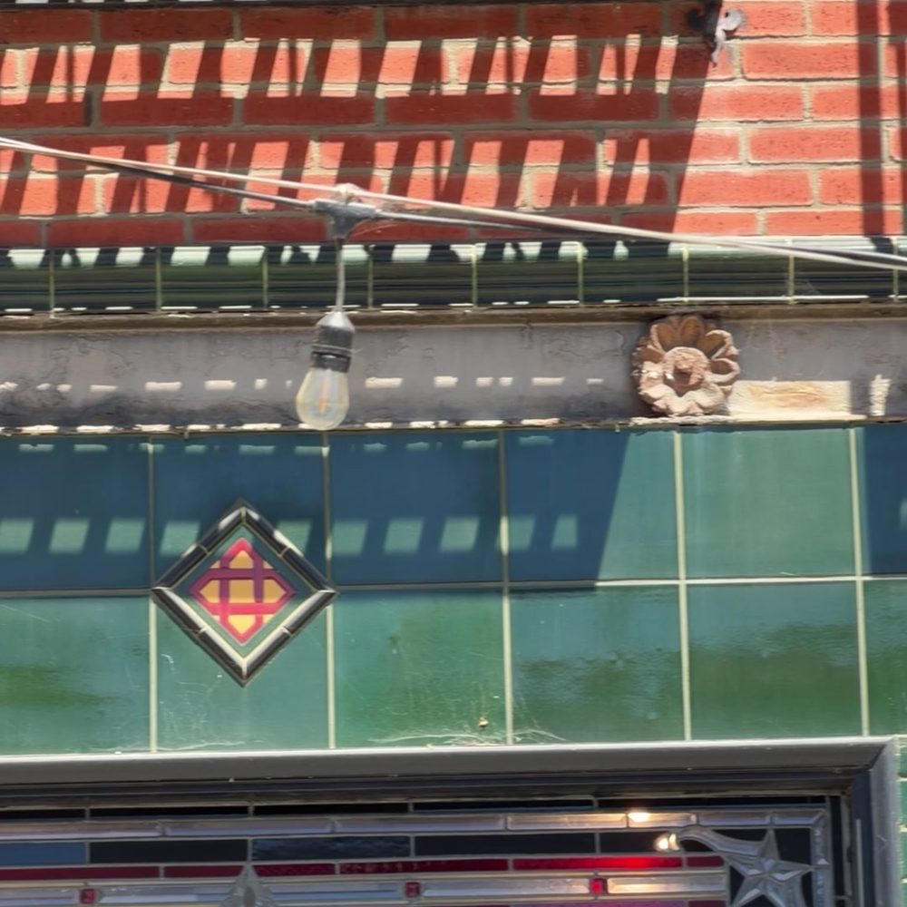 Close-up of green glazed tile with an orange and red diamond, above a leaded glass panel.