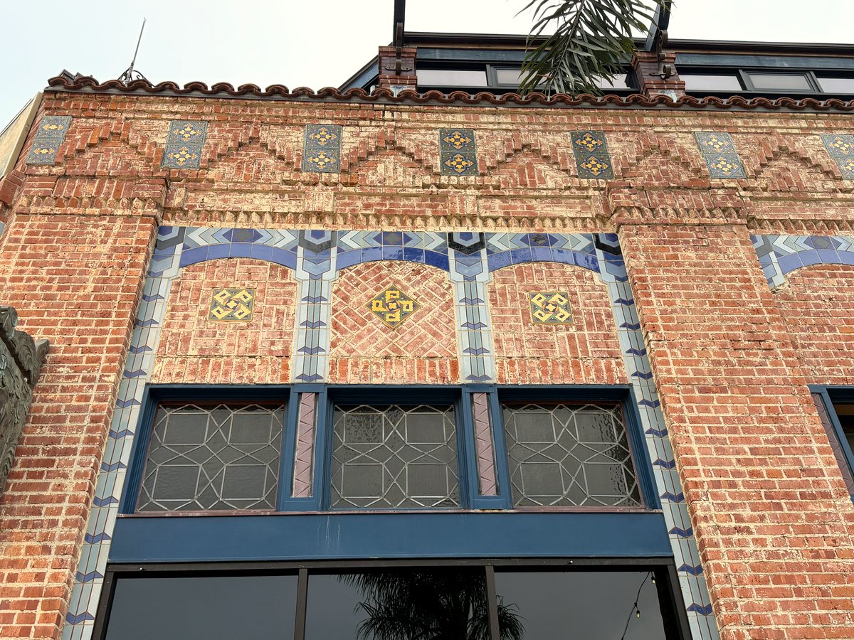 Close-up of the Watermark building facade: three blue tile arches with gold tile medallions set into patterned brick, above leaded windows.