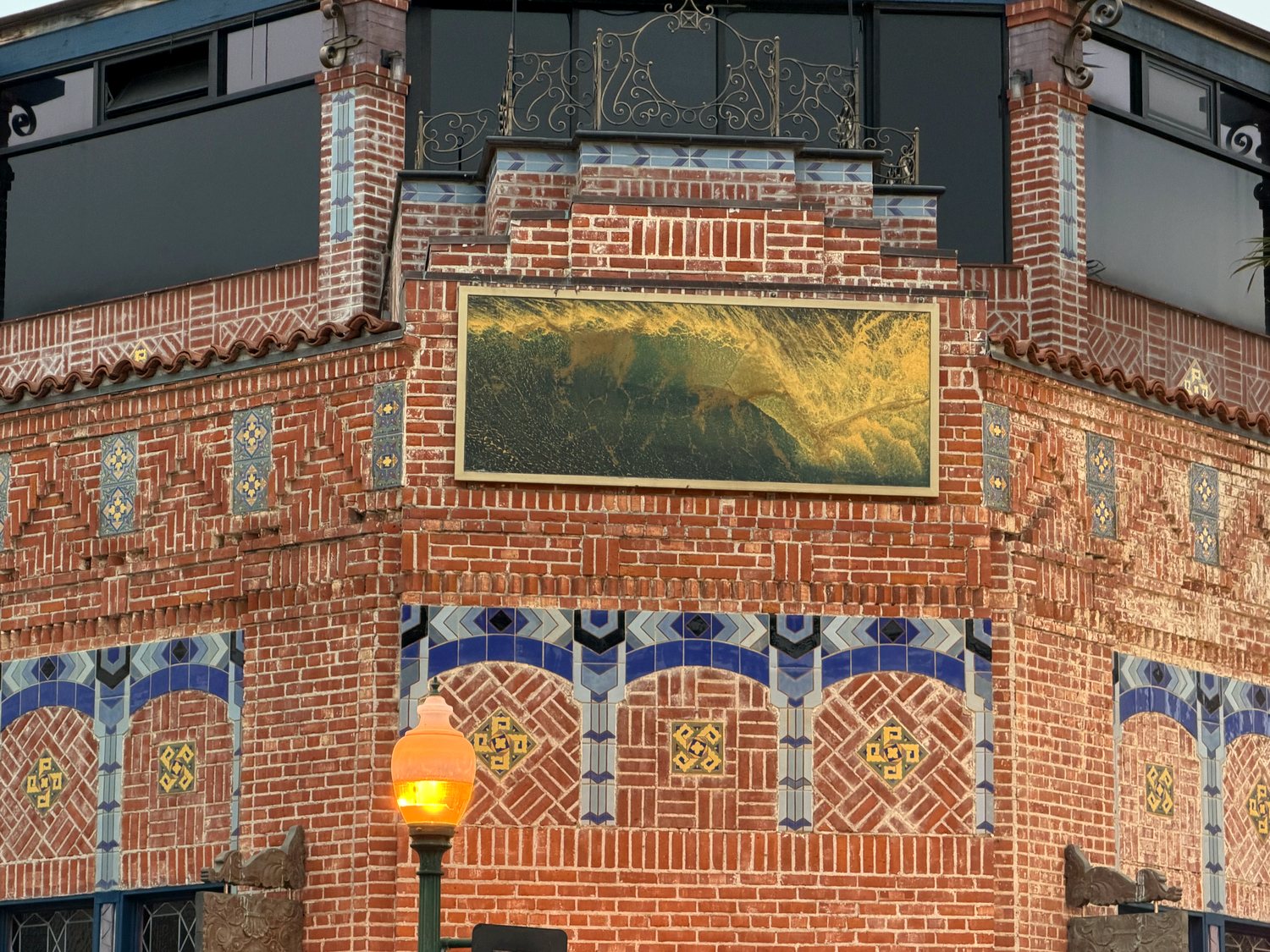 The top of the Watermark corner: a gilded panel under iron cresting, above blue tile arches set into patterned brick.