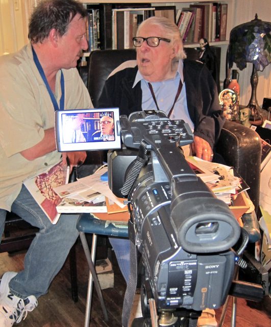 Michael O'Kelly filming Ray Bradbury at home, with a video camera on a tripod.