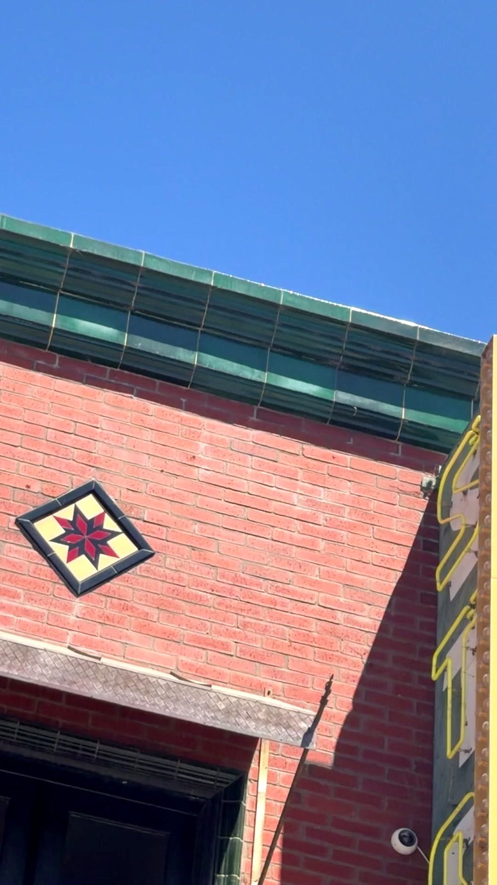 A star tile, an eight-pointed star in red and black on a yellow diamond, set into the red brick below the green tile cornice.
