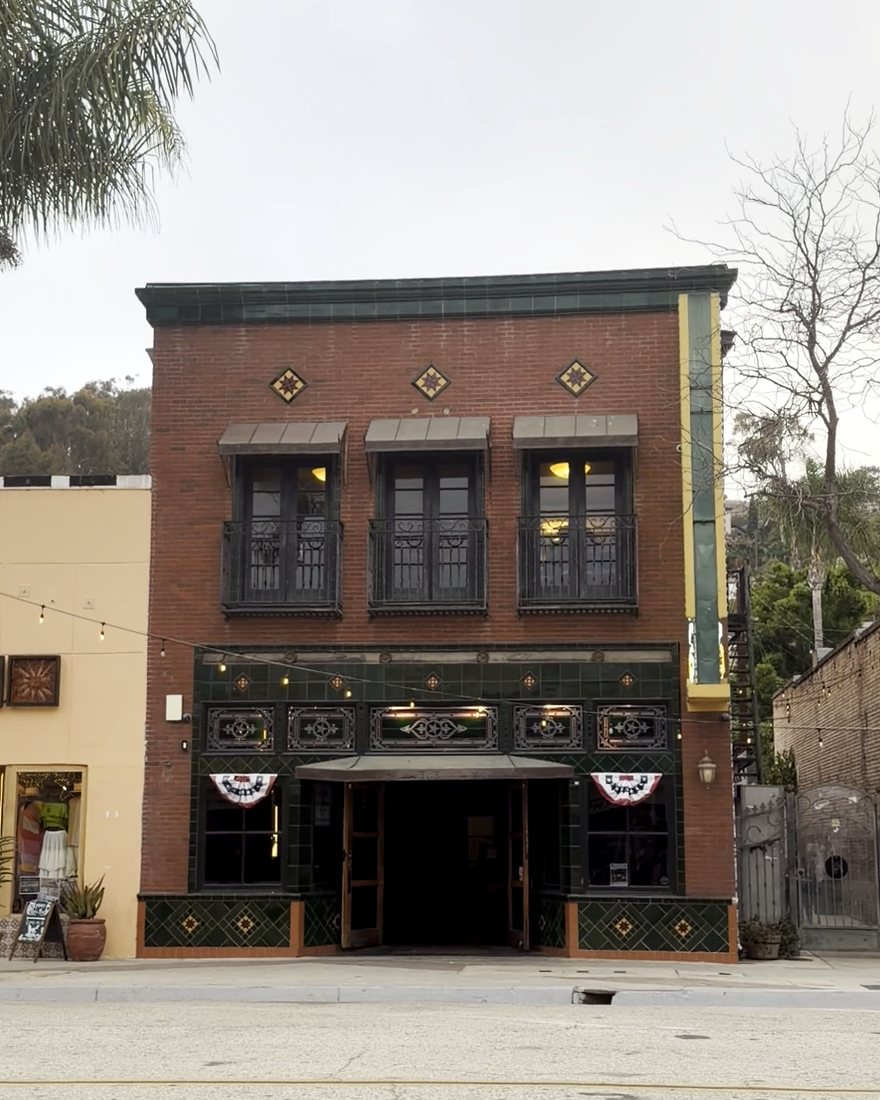The Star Lounge seen from across Main Street: a red brick and green tile front between a pale stucco shop and a bare tree, standing out on the block.