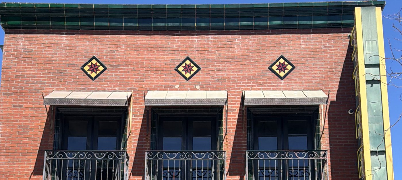 The top of the Star Lounge against a blue sky: a cap of green glazed tile along the roofline and three star tiles in the red brick above the balconies.
