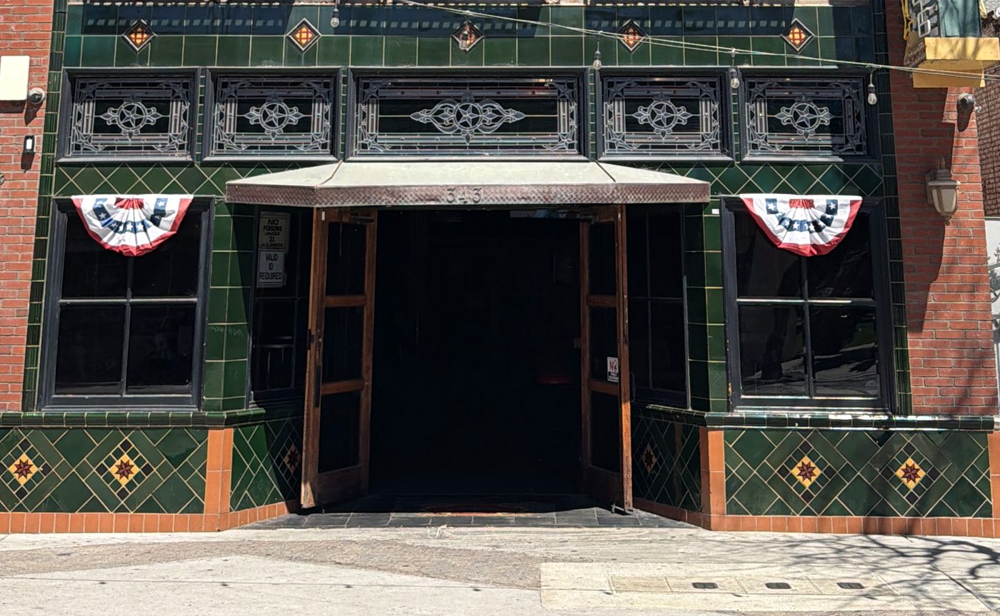 The Star Lounge shopfront in full sun: bottle-green glazed tile around the windows and the open door, a green band with diamonds above, and green and orange diamond panels at the base.