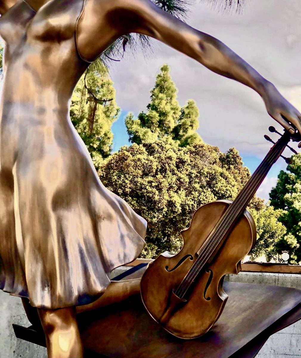 Detail of the bronze dress in motion and the violin, with the patina catching the sun.