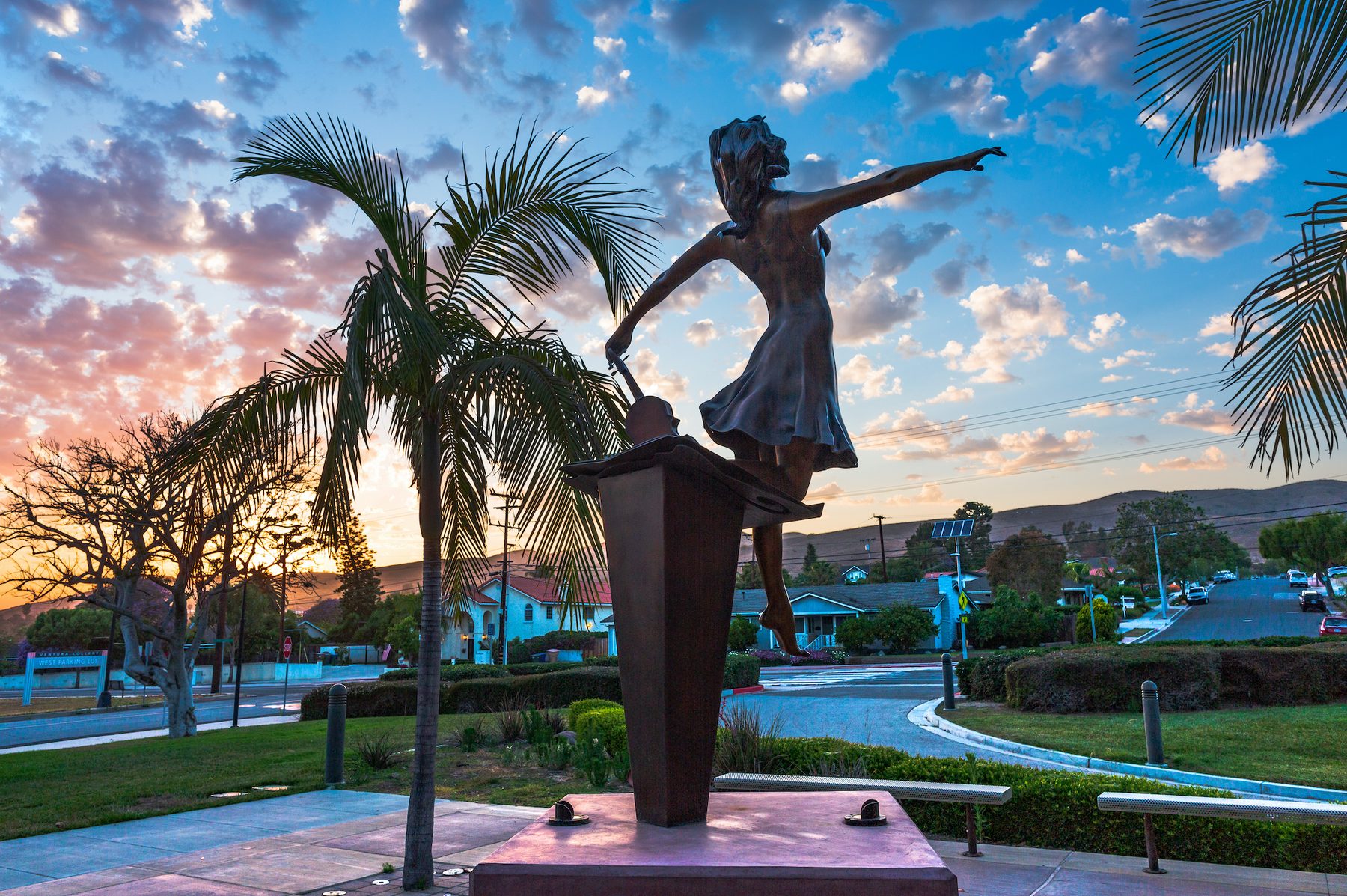 The bronze dancer on her plinth at the edge of the plaza, with palm trees and a sunset sky behind.