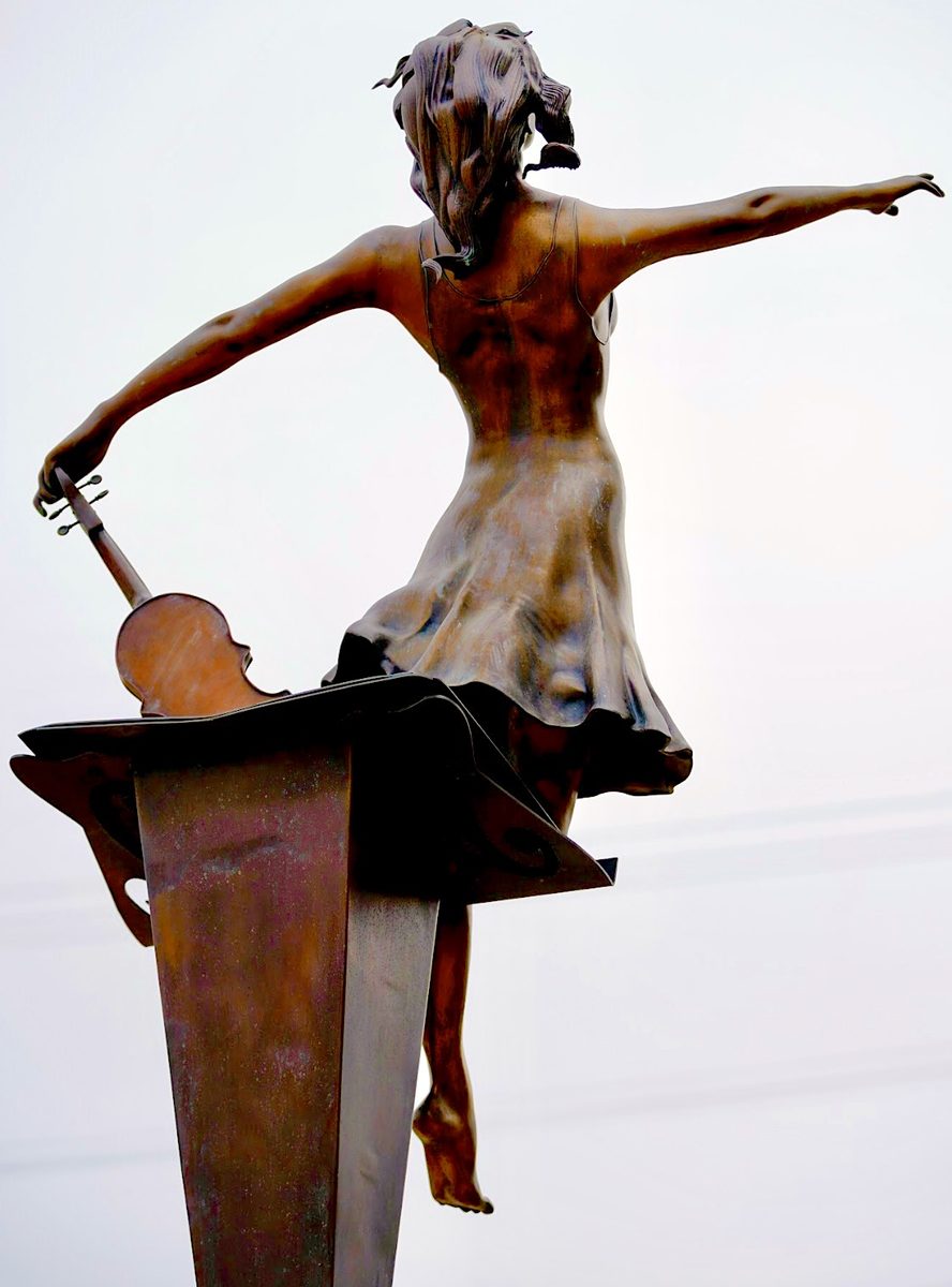 The dancer in profile, balanced above a music stand with a violin and bow.
