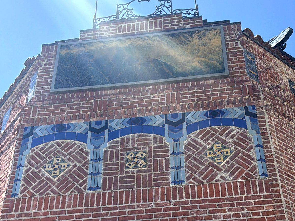 Looking up at the Watermark corner: blue tile arches and diamond patterns in the brick, under the gilded panel.