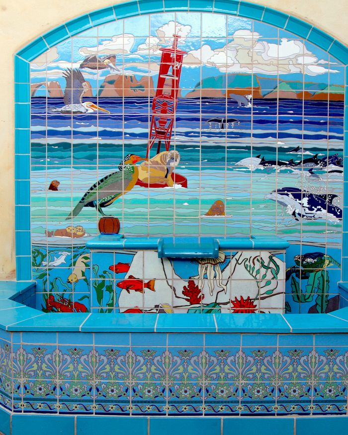 A tiled wall fountain in blues and turquoise: a pelican, a sea turtle, dolphins and a heron above an arched basin bordered with a patterned band.